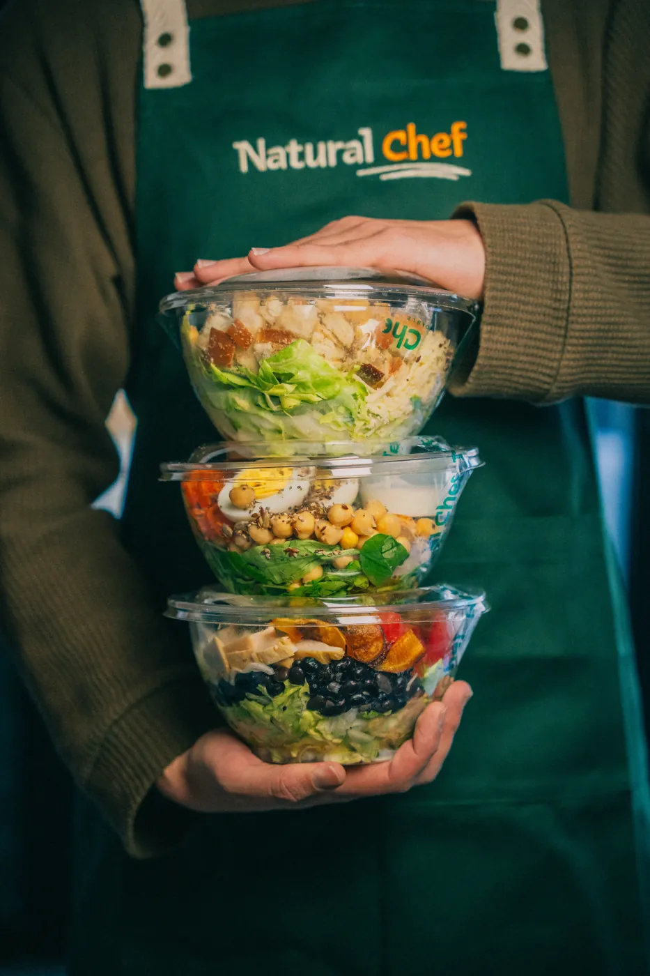Integrante del equipo de Natural Chef con tres bowls de ensalada apilados
